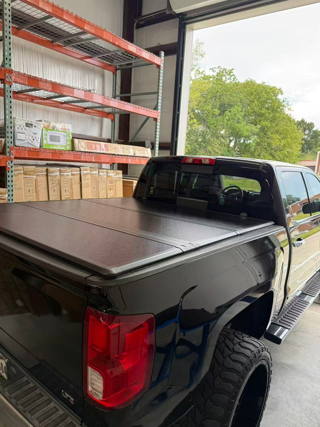 Installed hard tri-fold tonneau cover on a black pickup truck inside a workshop