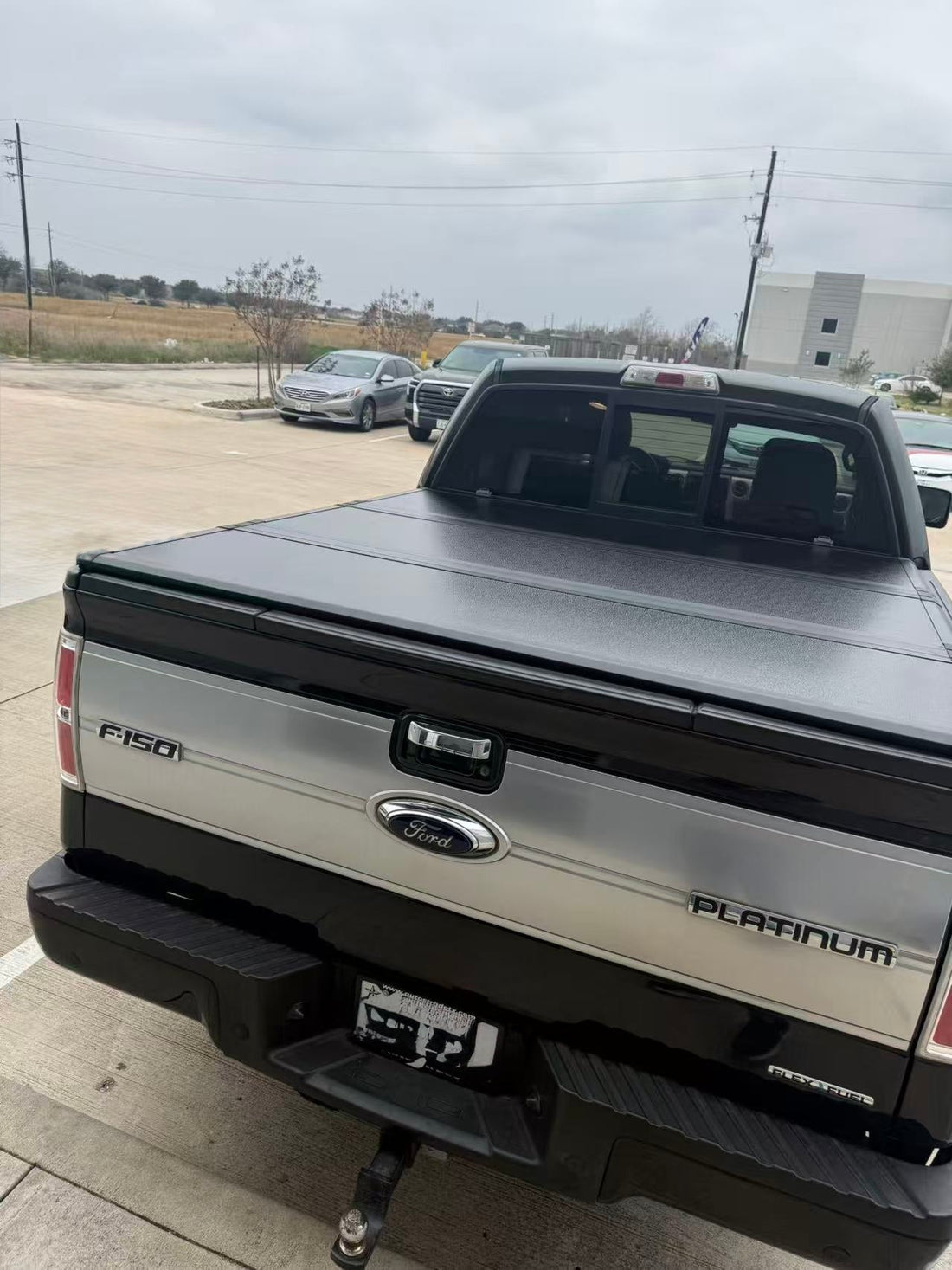 Closed hard tri-fold tonneau cover installed on a light-colored Ford pickup truck
